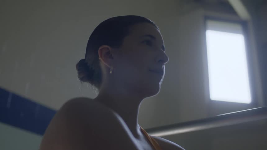 A woman is seated still in a platform with handrails inside a room as sun light shine in through the window