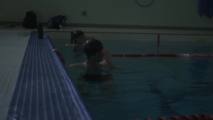 Male swimmers adjust swim goggles while floating in separate lanes in swimming pool