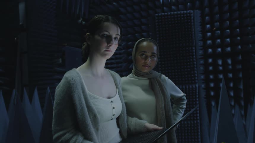 Two woman are standing in a room with sound reducing foam lining the walls