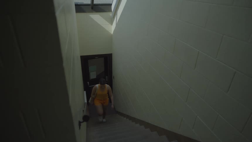 A woman in orange walks up a flight of stairs and turns right at the top