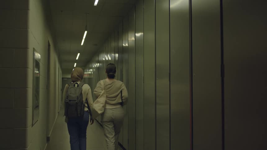 Two women walking together travel down a long hallway