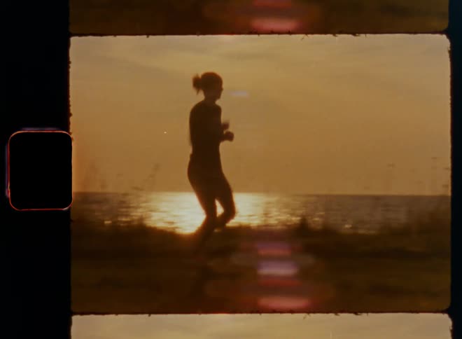 Panning shot of silhouette of a young female fitness coach or jogger wearing sports clothing that runs along a path next to the ocean on a sunny day during her morning exercising workout as her healthy daily routine and cardio training to lose weight