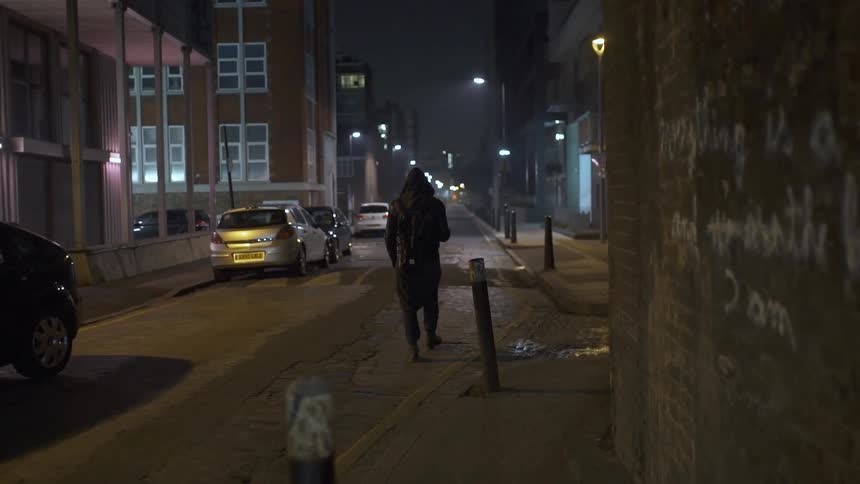 A man is walking down a city street at night