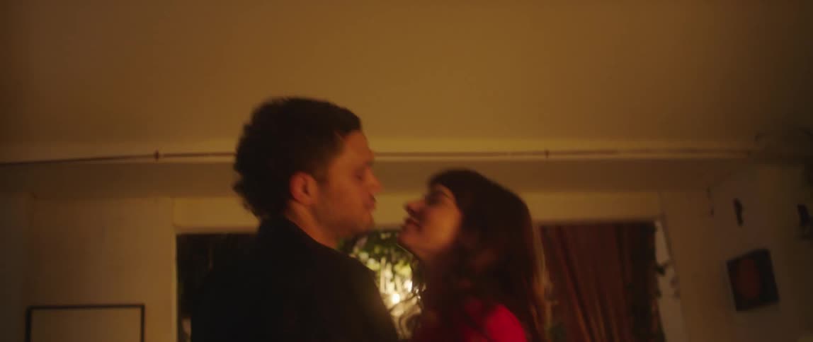 Young couple dancing together and kissing each other while the woman is holding a glass of wine in the middle of the living room at night