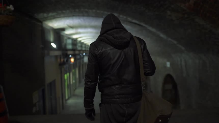 A man is walking towards a tunnel with a bag