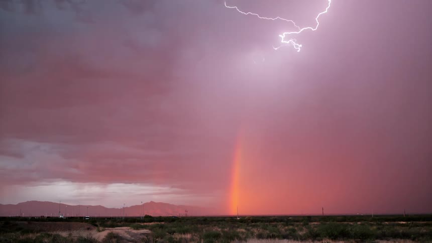 Thunder and lightning storm creates bright rainbow near town and mountains