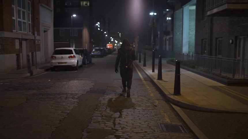 A man is walking down a city street at night