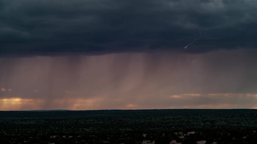 Rain falls from dark storm clouds as a bolt of lightning strikes the ground