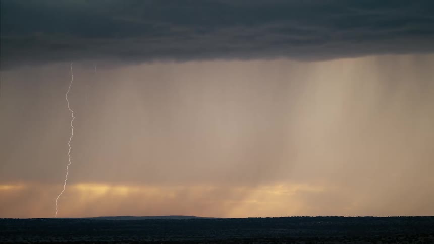 A lightning bolt striking down from the sky during a thunderstorm on a wide open landscape