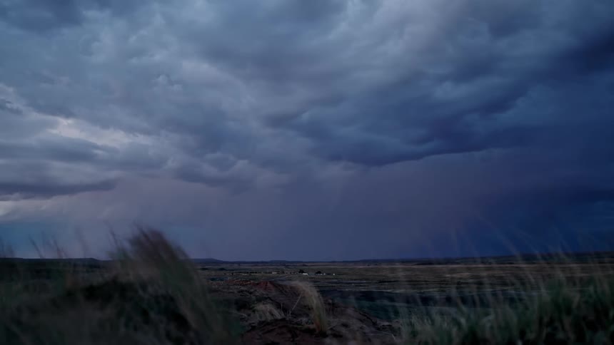 Lightning flashes beneath thick storm clouds over a grassy plain