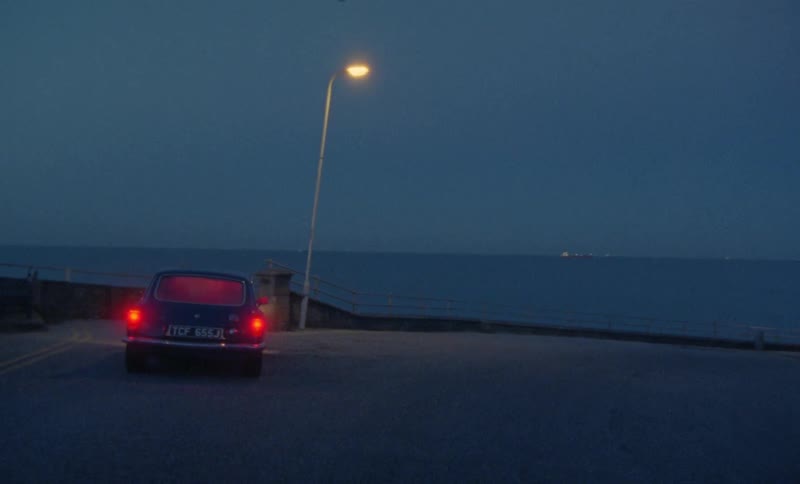 A car pulling into a parking lot and parking in front of a light post in front of the ocean front