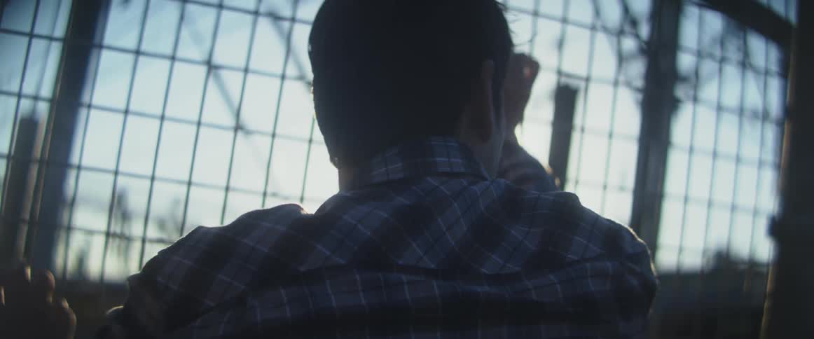 A man grips a wire fence as he looks out beyond the fence