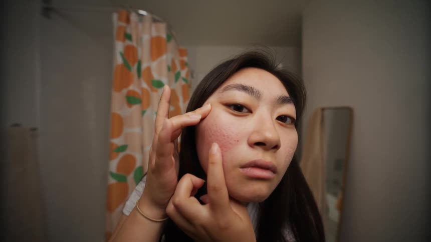 A woman inside the bathroom checking her face for pimples