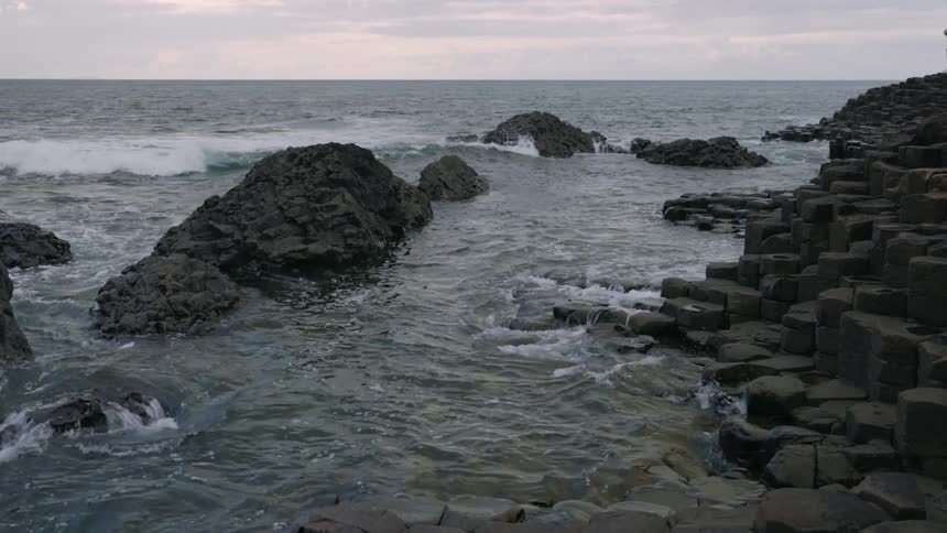 The waves from the sea crash onto the rocky shoreline during sundown