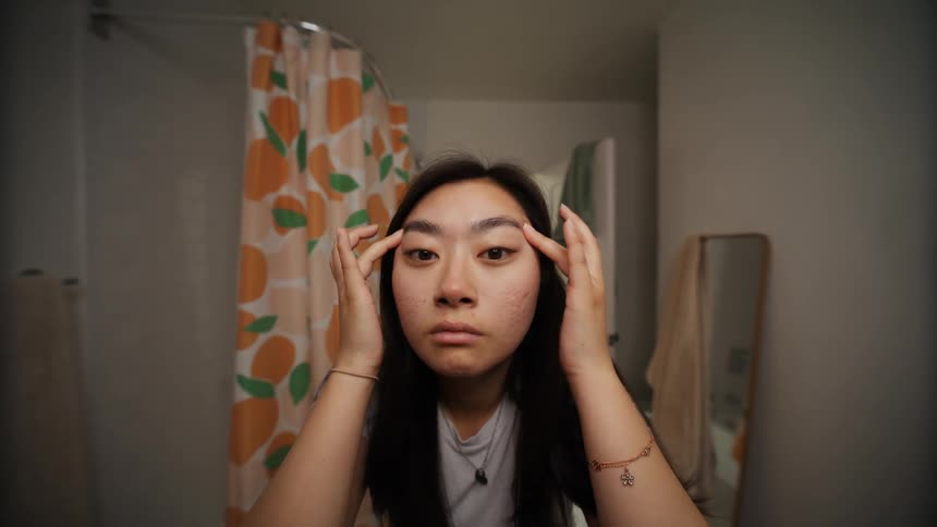 A young woman fiddling with her nose and eyebrows trying to figure out how she would like her look better