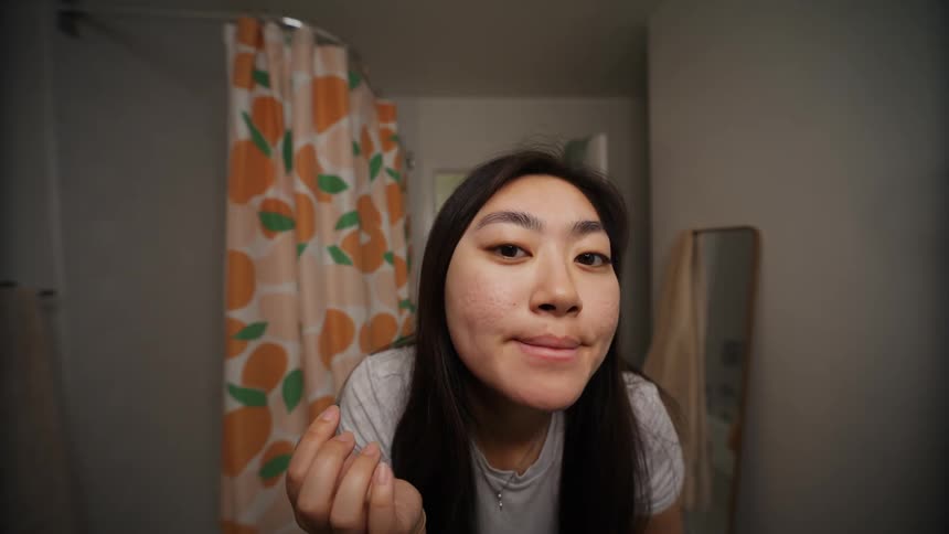 A woman leans forward to inspect her reflection in the bathroom mirror