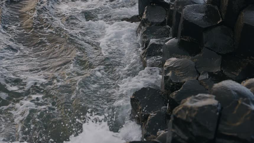 Waves crashing against the rocky coastline as foam forms on the surface