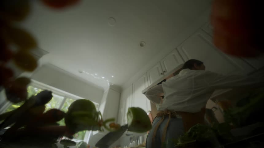Woman with apron and shirt cuts vegetable and making a dish in the kitchen