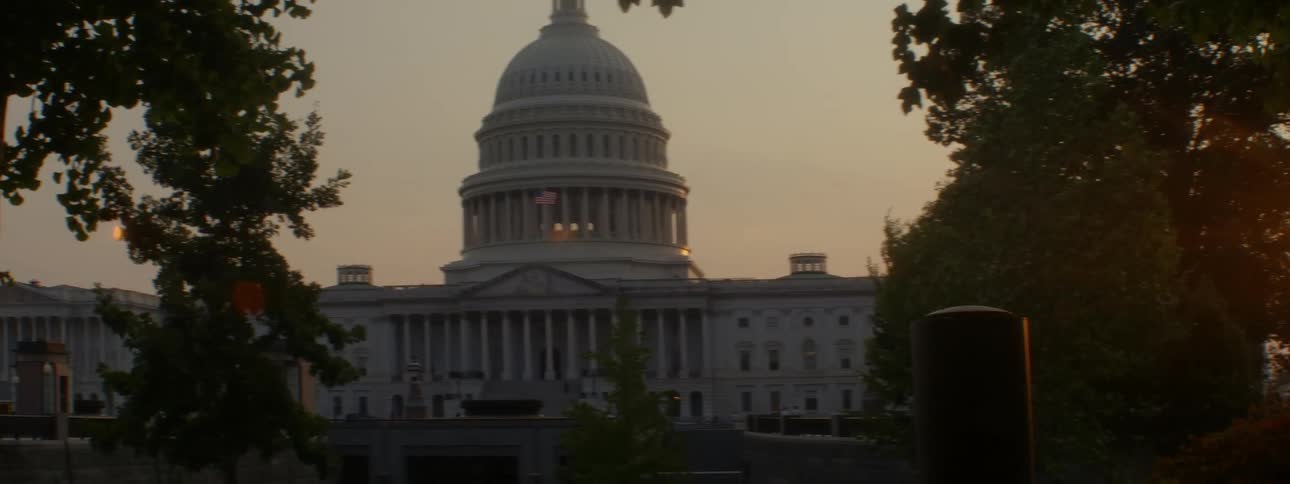 Sun setting through trees blowing in the wind near the capitol building in the evening