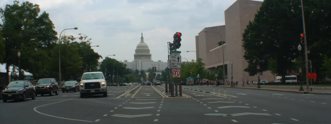 Cars turning at an intersection near traffic signs with the capitol building in the background