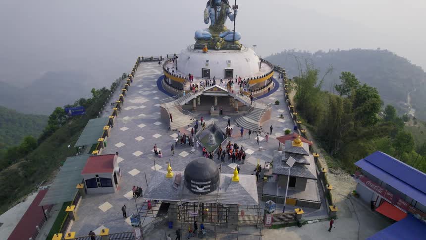 An aerial view of a mountain top with a statue and people passing by
