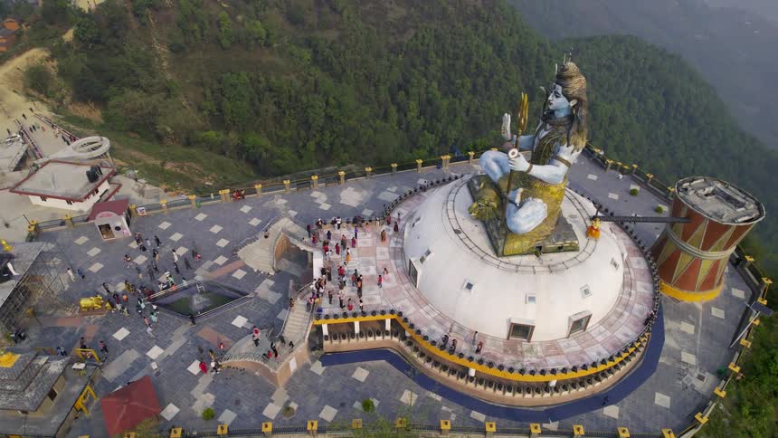 A huge statue holding a trident on a platform in a montanah full of tourists