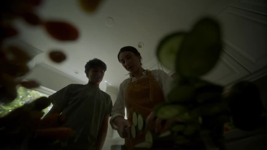 A boy watches his mother cut vegetables