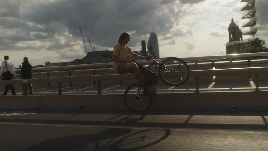 Cyclist performs extended wheelie on bicycle as he rides across one of several bridges in the city on sunny day