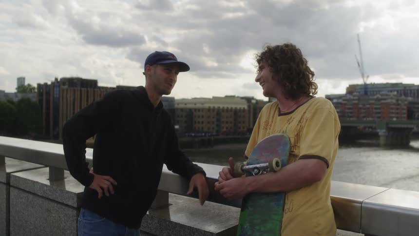 Two men talk while leaning against rail of bridge spanning busy river