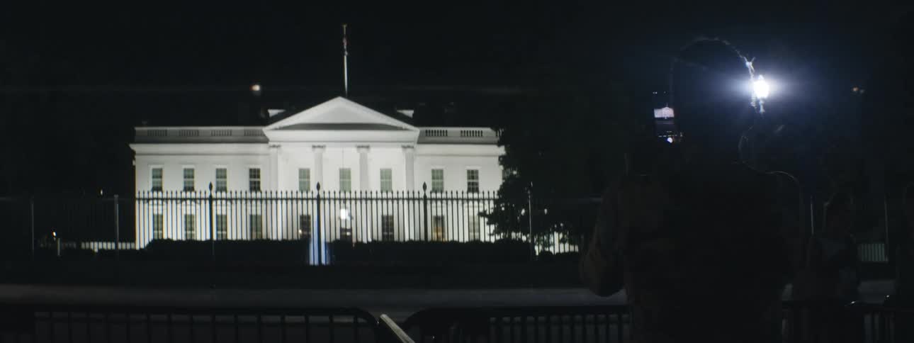 A woman taking a picture of the white house in washington dc at night with lights displayed on the white house