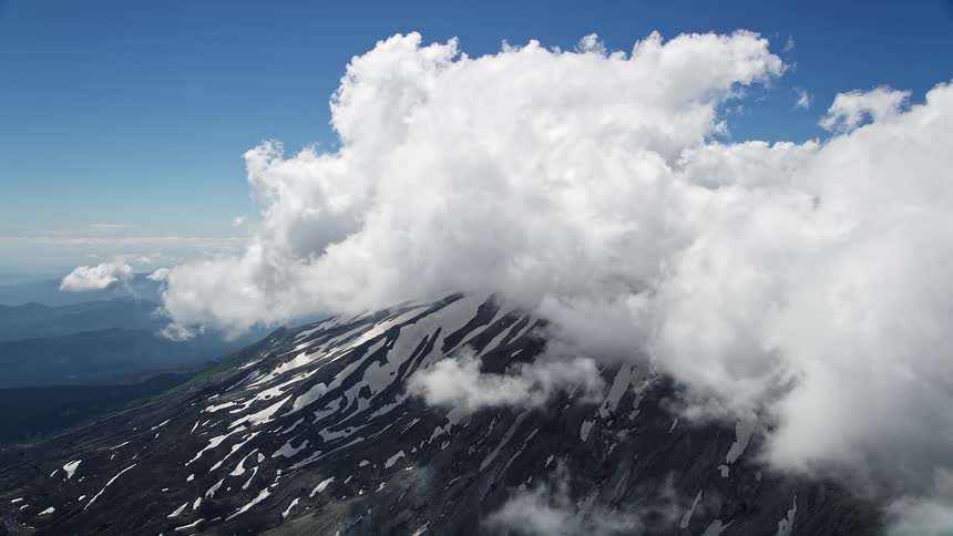 Aerial footage of Mount St Helens covered in snow surrounded by low clouds showcasing the majestic beauty of the Washington wilderness