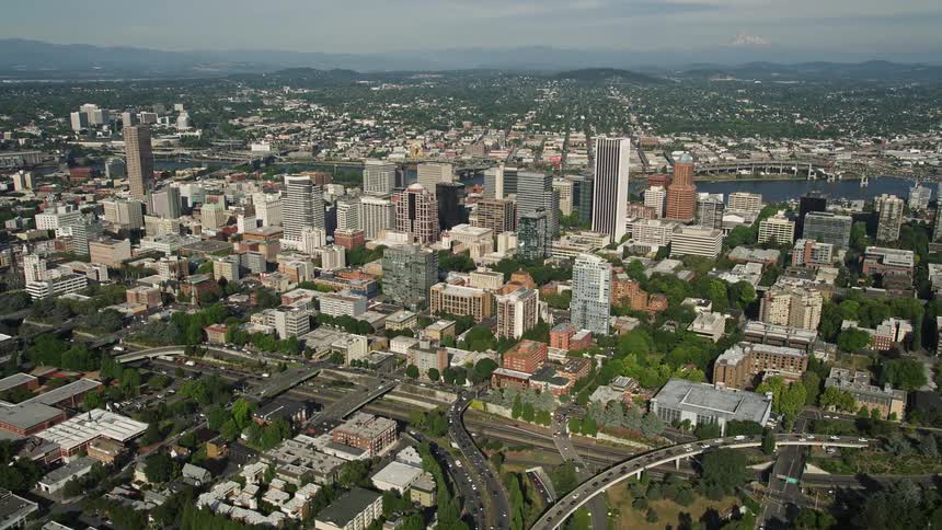 Aerial footage of downtown Portland Oregon during a sunny day showing high rise buildings and skyscrapers as traffic runs through the city streets