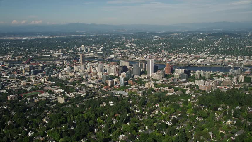  aerial footage flying over downtown Portland Oregon with tall buildings lining the river on a sunny day