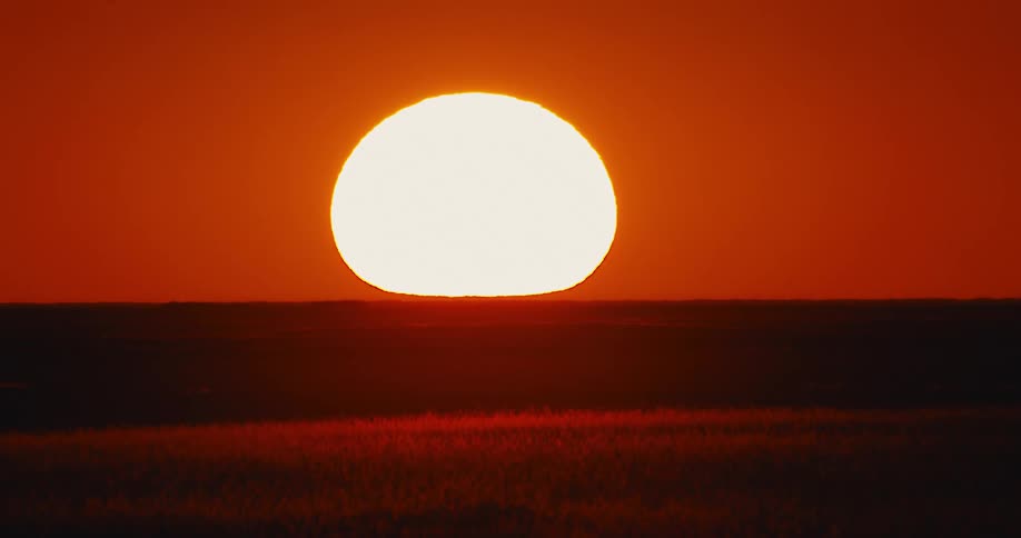 Sun rises in red sky over a dark landscape