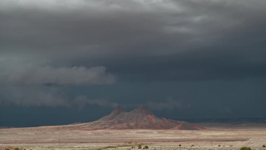 Lightning illuminates area behind mountains surrounded by desert
