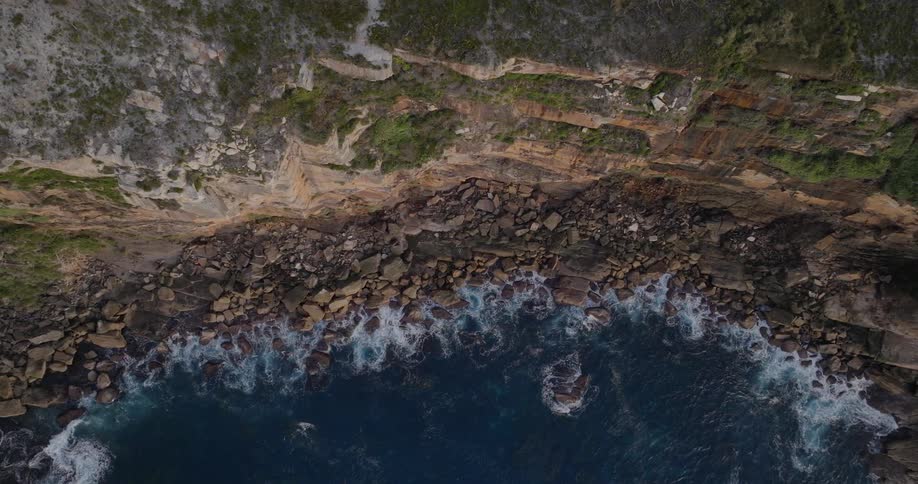 In midday at shore the waves hit the shoreline filled with rocks with a small village close by