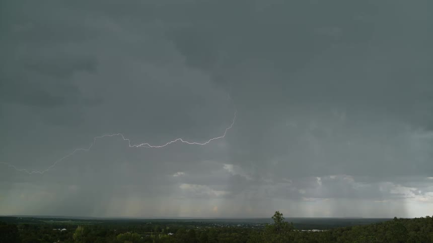Lightning flashes and moves across the sky over a town and strikes the ground
