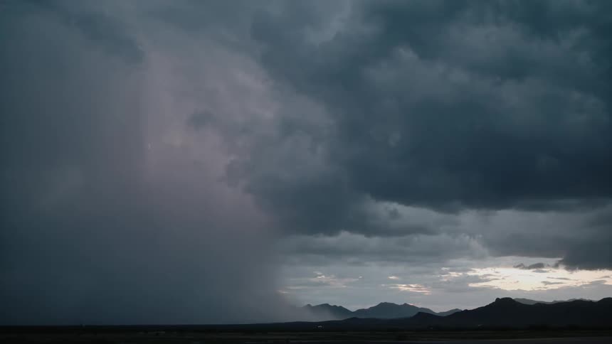 Dark storm clouds move over mountainous terrain pouring rain as lightning strikes the ground