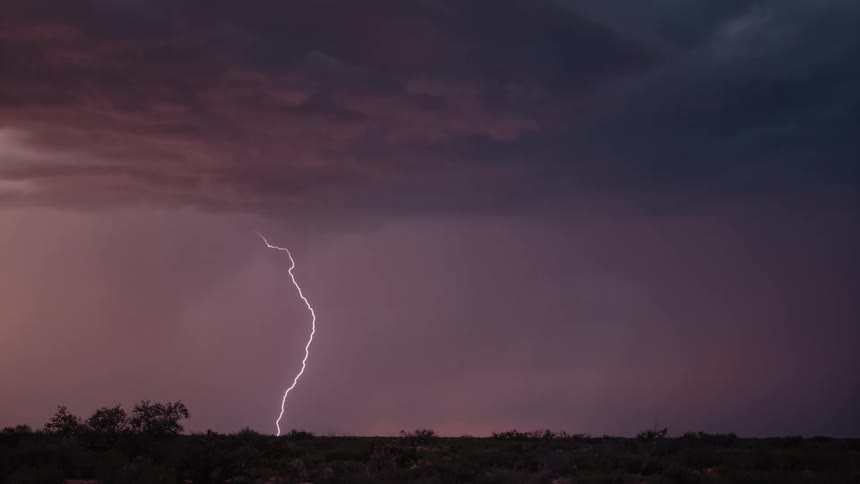 Lightning striking the ground and lighting up the pink and purple cloudy sky with silhouette horizon landscape