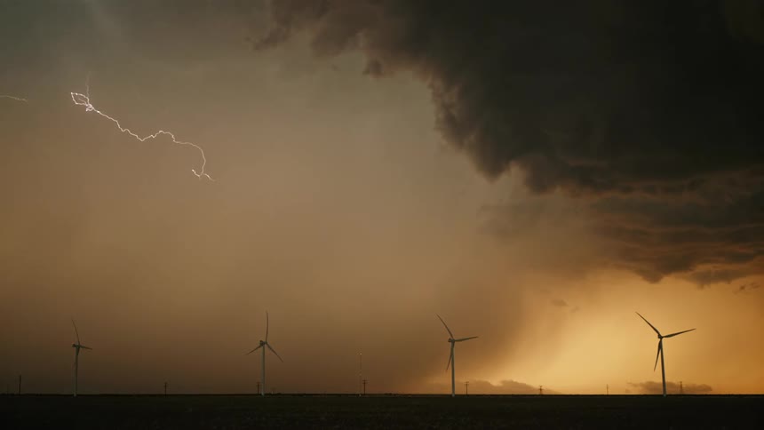 Windmills turning in the wind as lightning strikes the orange burnt sky