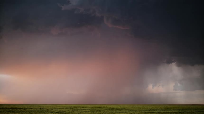 Lightning strikes in slow motion from a huge black cloud onto an empty field