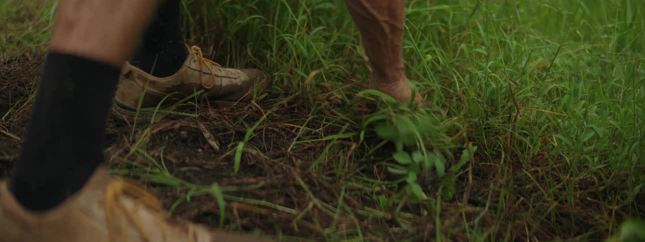 Close up of a man pulling weeds from the ground as he is bent over on a bright day
