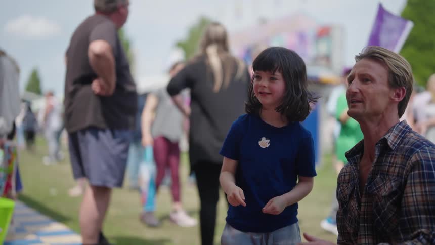 A young girl standing next to her father as she throws a dart and he hands her another one to throw