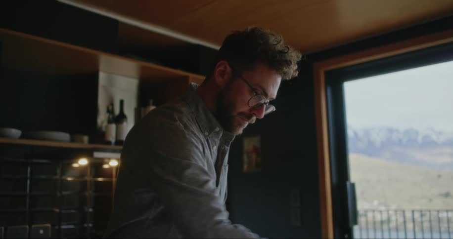 Man working on the computer and preparing a vegetable in the kitchen