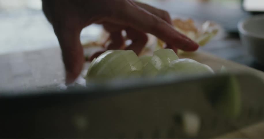 A person cuts an onion with a large knife on top of a wooden board