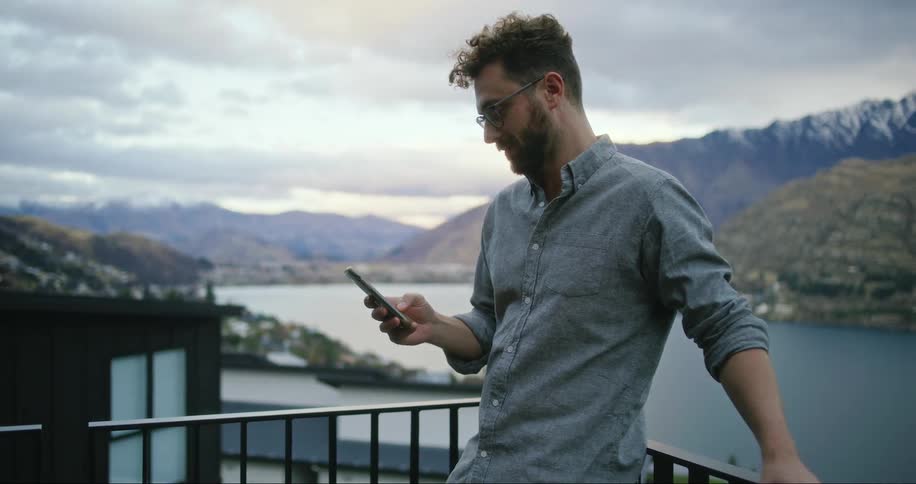 A man on a scenic balcony with his back to the view checking his smart phone