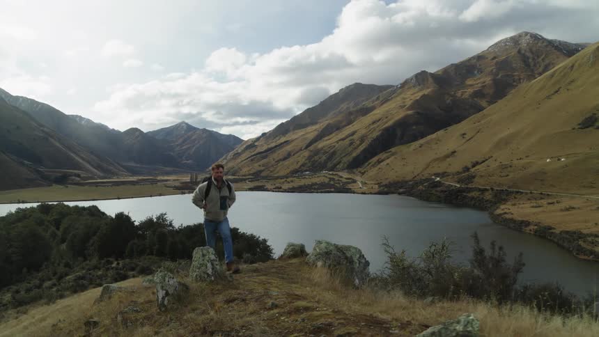 Man walking on hills near a river and mountains