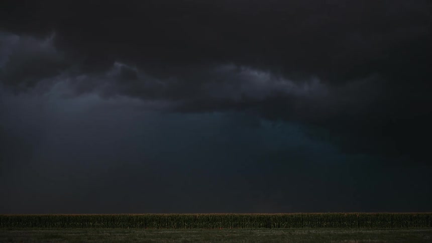 A thunderstorm with lightning lighting up the dark night sky above a flat field below