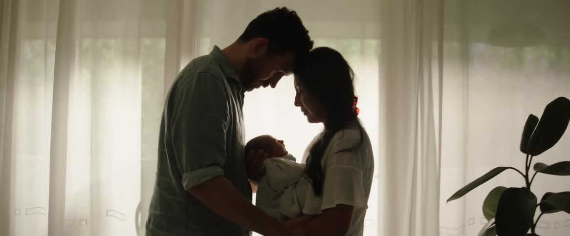 A man and a woman with their heads together as they hold a baby in their lap