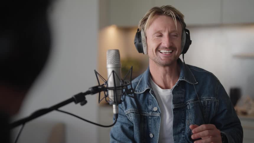 A man wearing headphones talking into a microphone while talking to someone in front of him